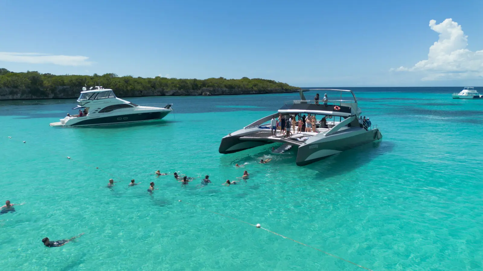 Power catamaran and motor yacht anchored off a wooded island near Punta Cana as guests swim nearby