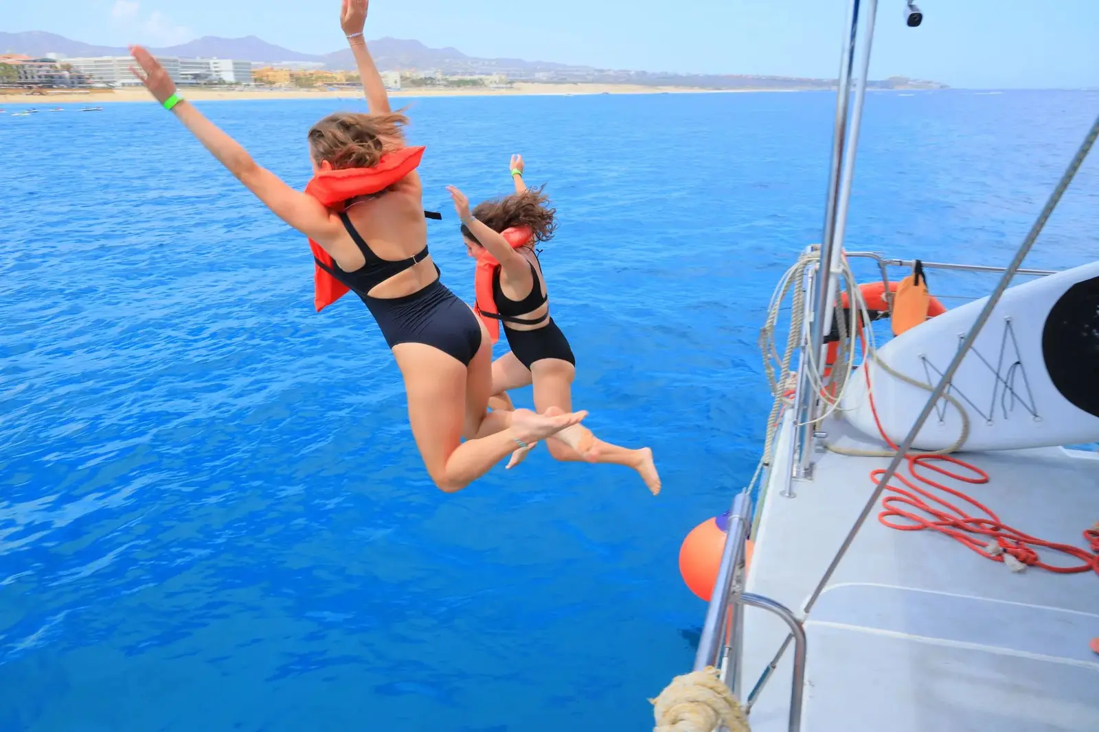 Two guests in life vests leap from the catamaran into blue water off the Los Cabos coast