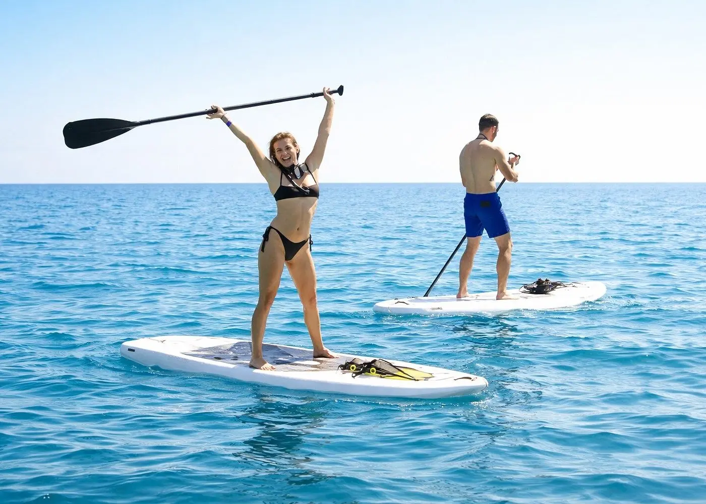 Woman lifts her paddle overhead on a stand-up paddleboard as a man paddles behind her off Los Cabos
