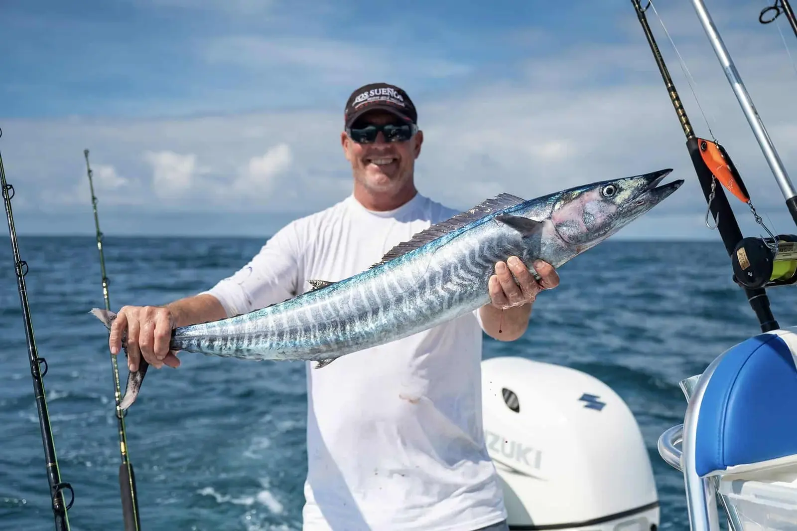 Smiling angler in a white sun shirt holding up a striped wahoo aboard a sportfishing boat