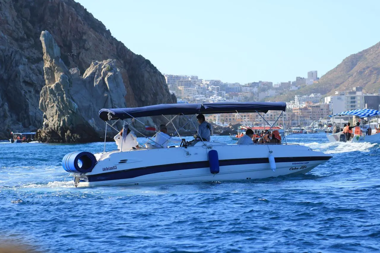 Small yacht with guests cruising across the bay with Cabo San Lucas hotels and hills behind