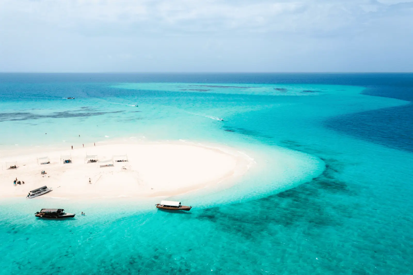 Aerial view of a curving white sandbank with wooden boats anchored in turquoise water off Zanzibar