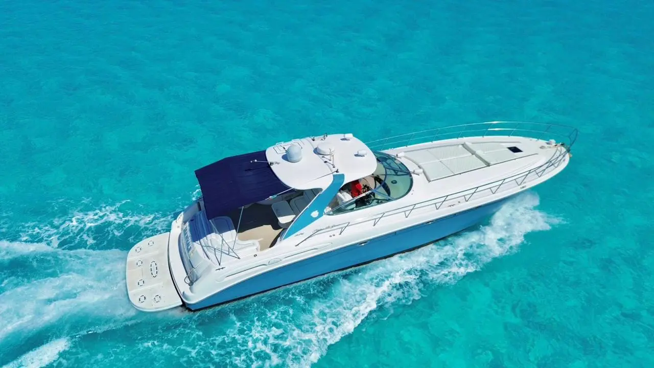 Drone view of a motor yacht with a navy canopy cruising across turquoise water
