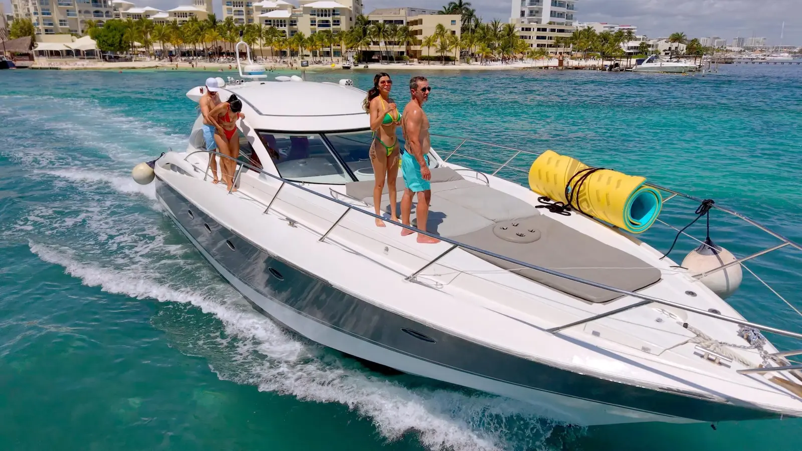 Guests standing on the bow of a motor yacht speeding past beachfront hotels in Cancún