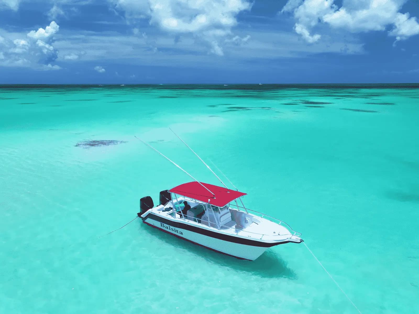 Speedboat with a red canopy anchored in shallow turquoise water near Saona Island
