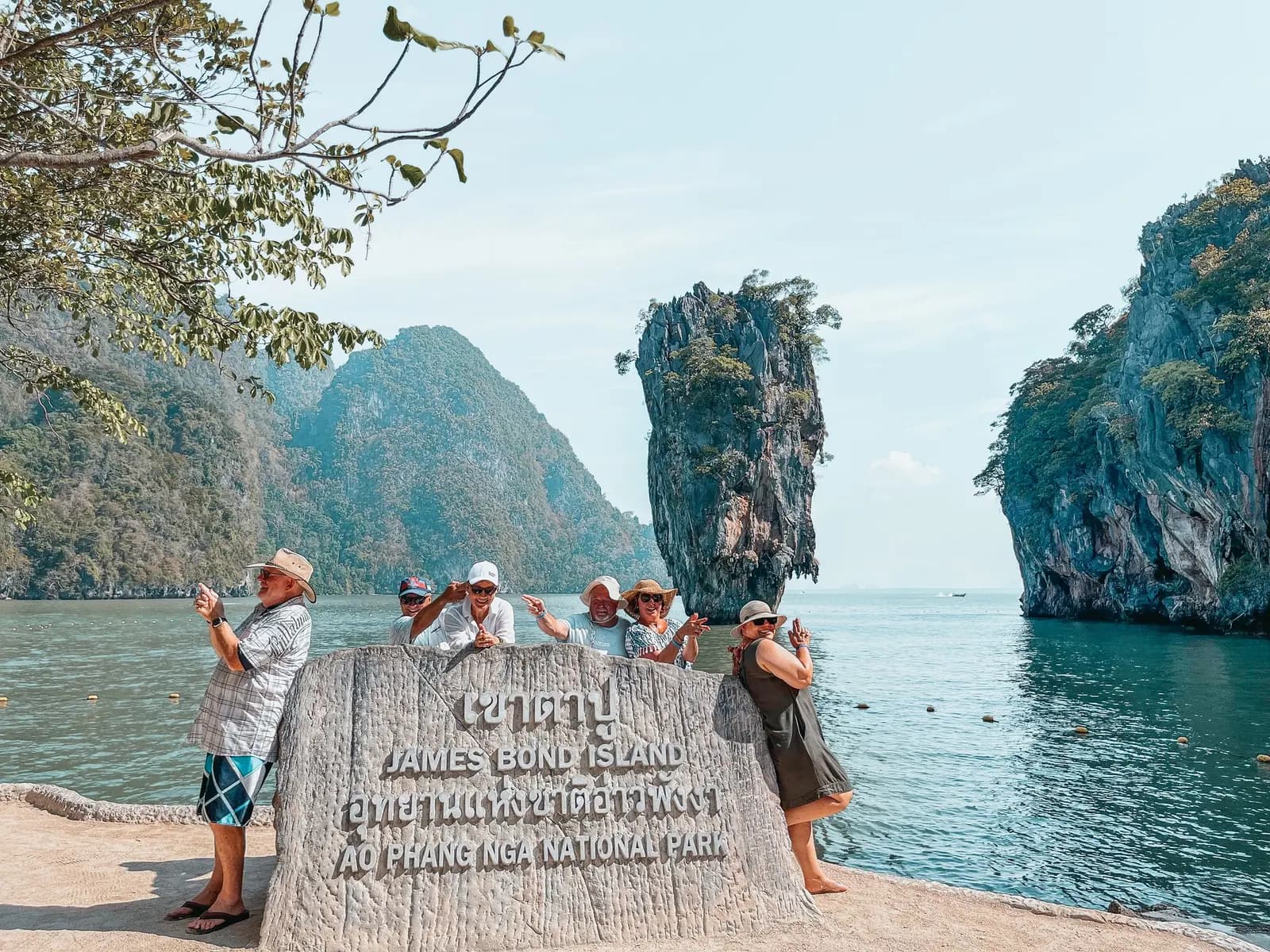 Visitors taking photos by the stone sign at Khao Phing Kan, the needle-shaped rock rising from the bay behind