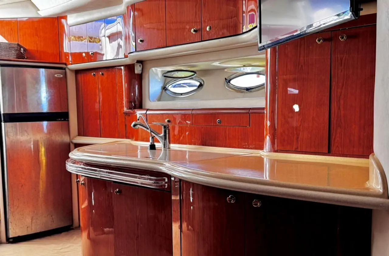 Galley with glossy cherry wood cabinets, a stainless steel fridge and portholes inside a motor yacht