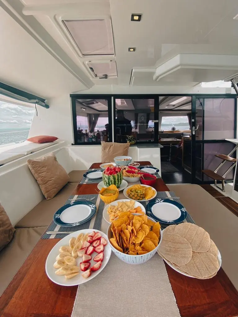 Saloon table on a sailing catamaran set with plates, fruit, tortilla chips and flatbread