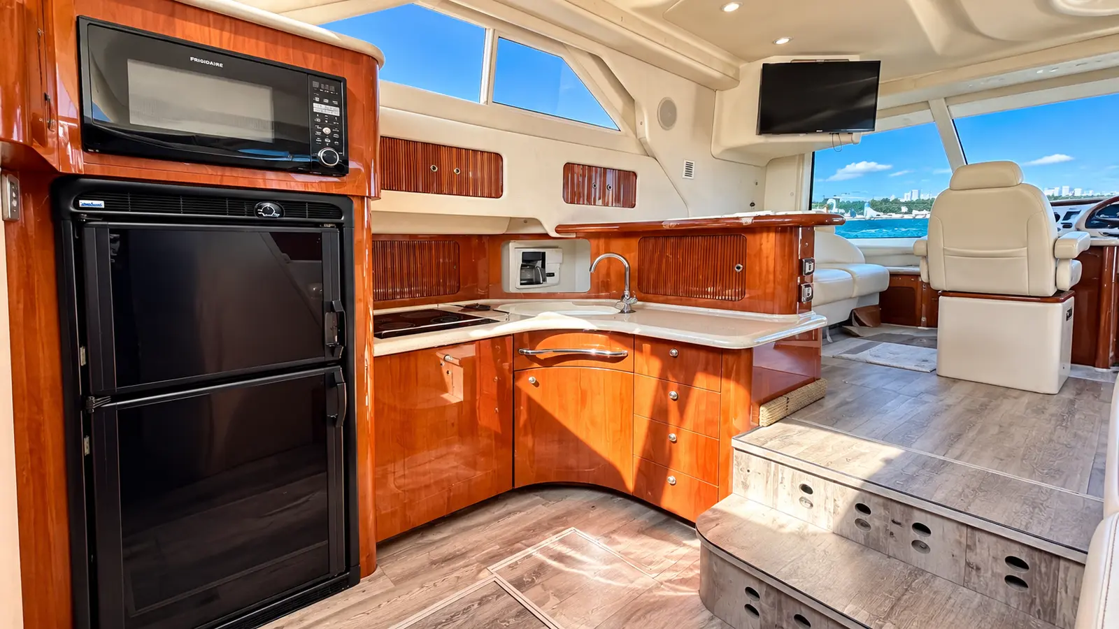 Galley with glossy wood cabinets, fridge and microwave next to the helm seat inside a yacht