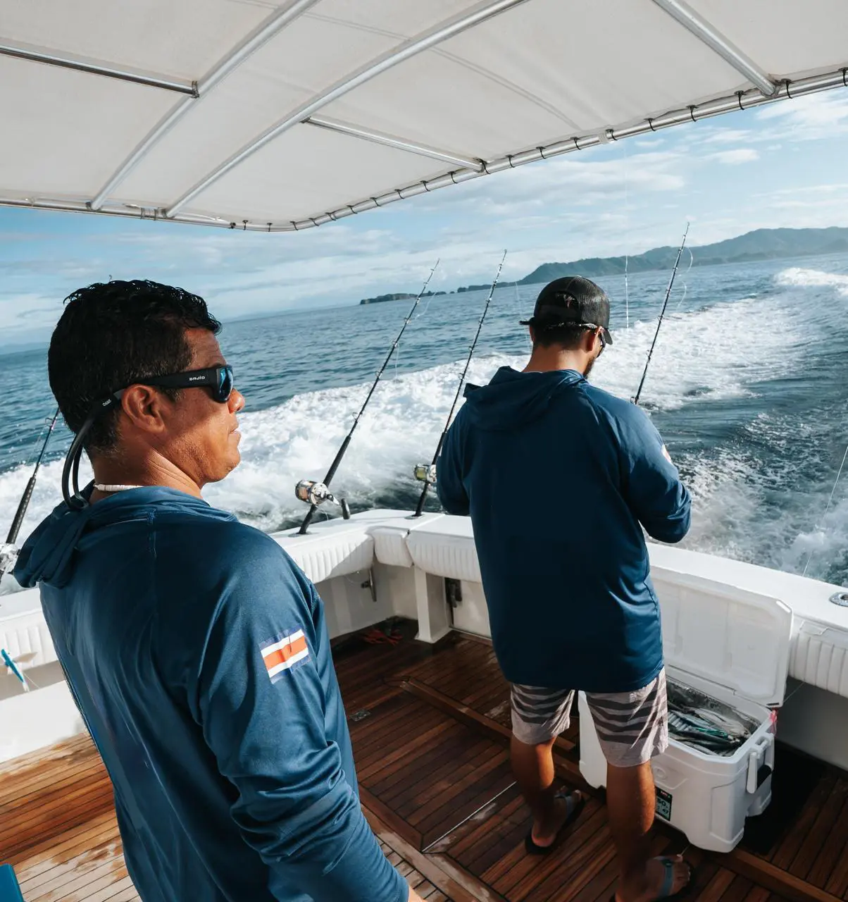 Two men in blue hooded shirts watching the trolling lines from the yacht's cockpit off the Costa Rica coast