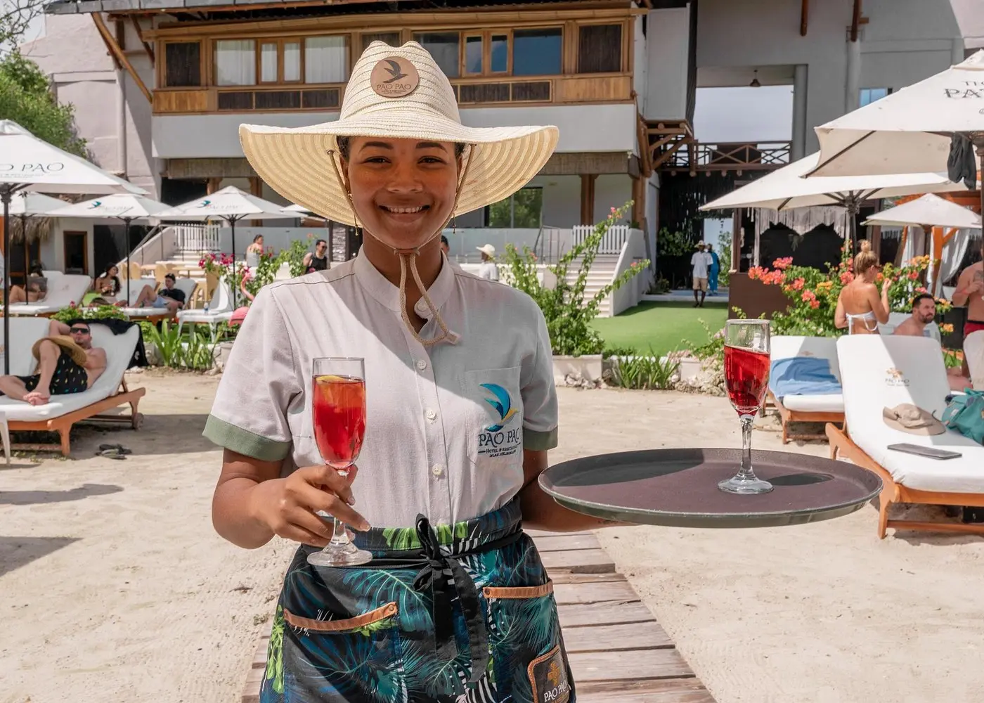 Smiling host in a straw hat offering red welcome drinks from a tray at a Rosario Islands beach club