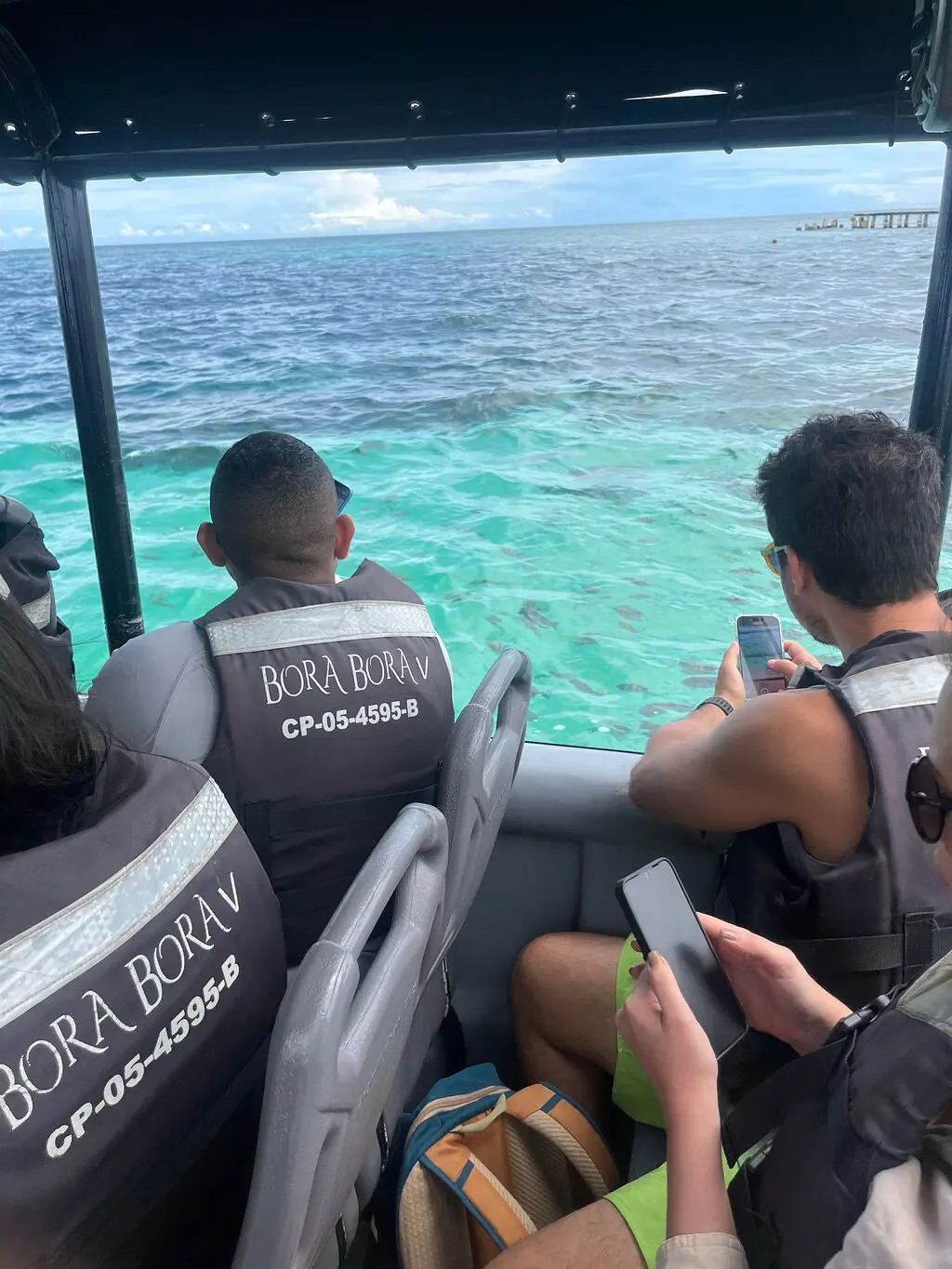 Guests in life jackets taking phone photos of the turquoise sea from the side of a speedboat