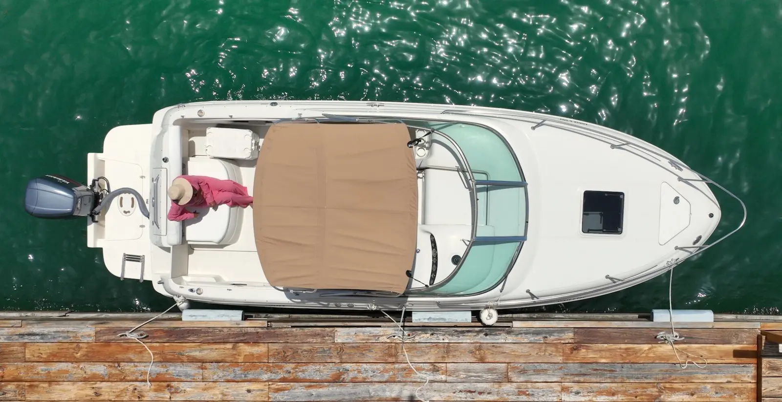 Top-down view of the motorboat moored at a wooden dock with a woman relaxing at the stern