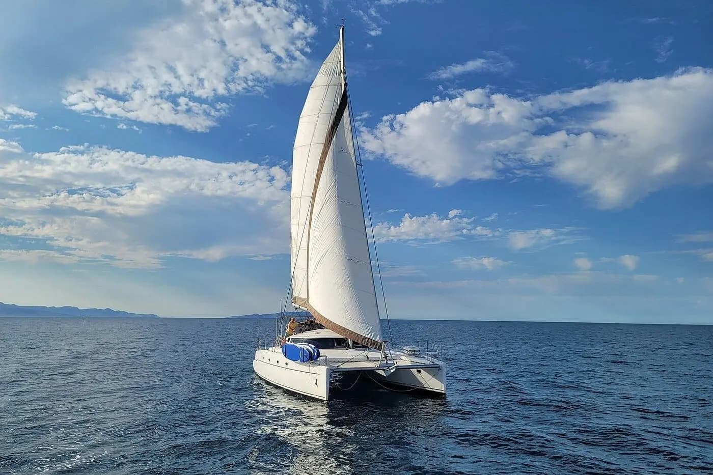 Sailing catamaran under full sail on the deep blue Sea of Cortez beneath puffy white clouds