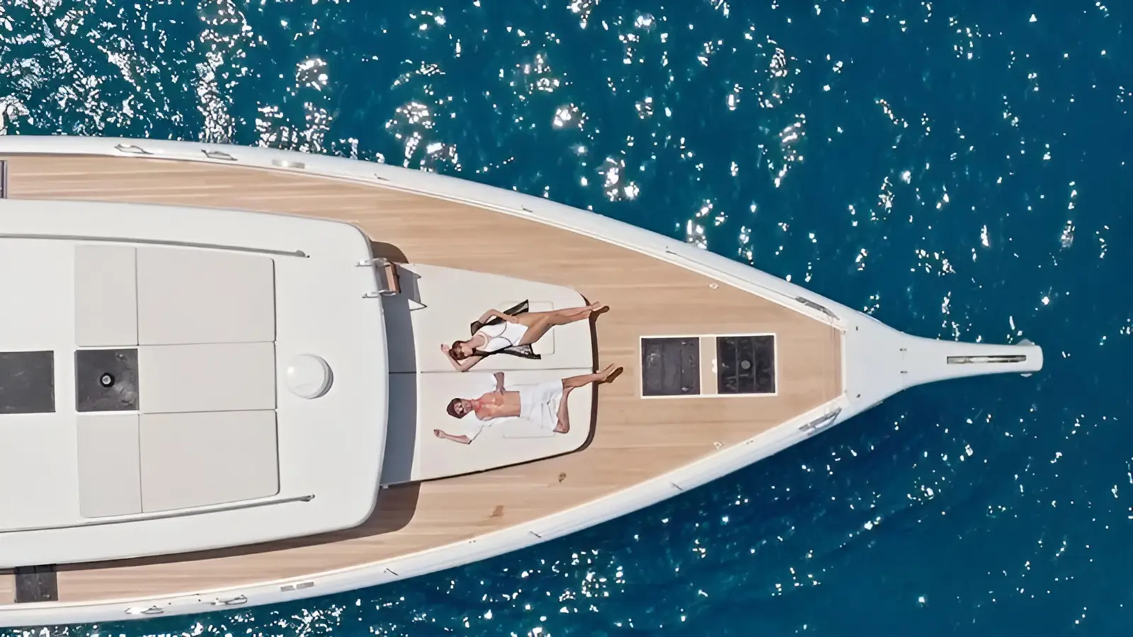 Overhead view of two guests sunbathing on the teak foredeck of the motor yacht