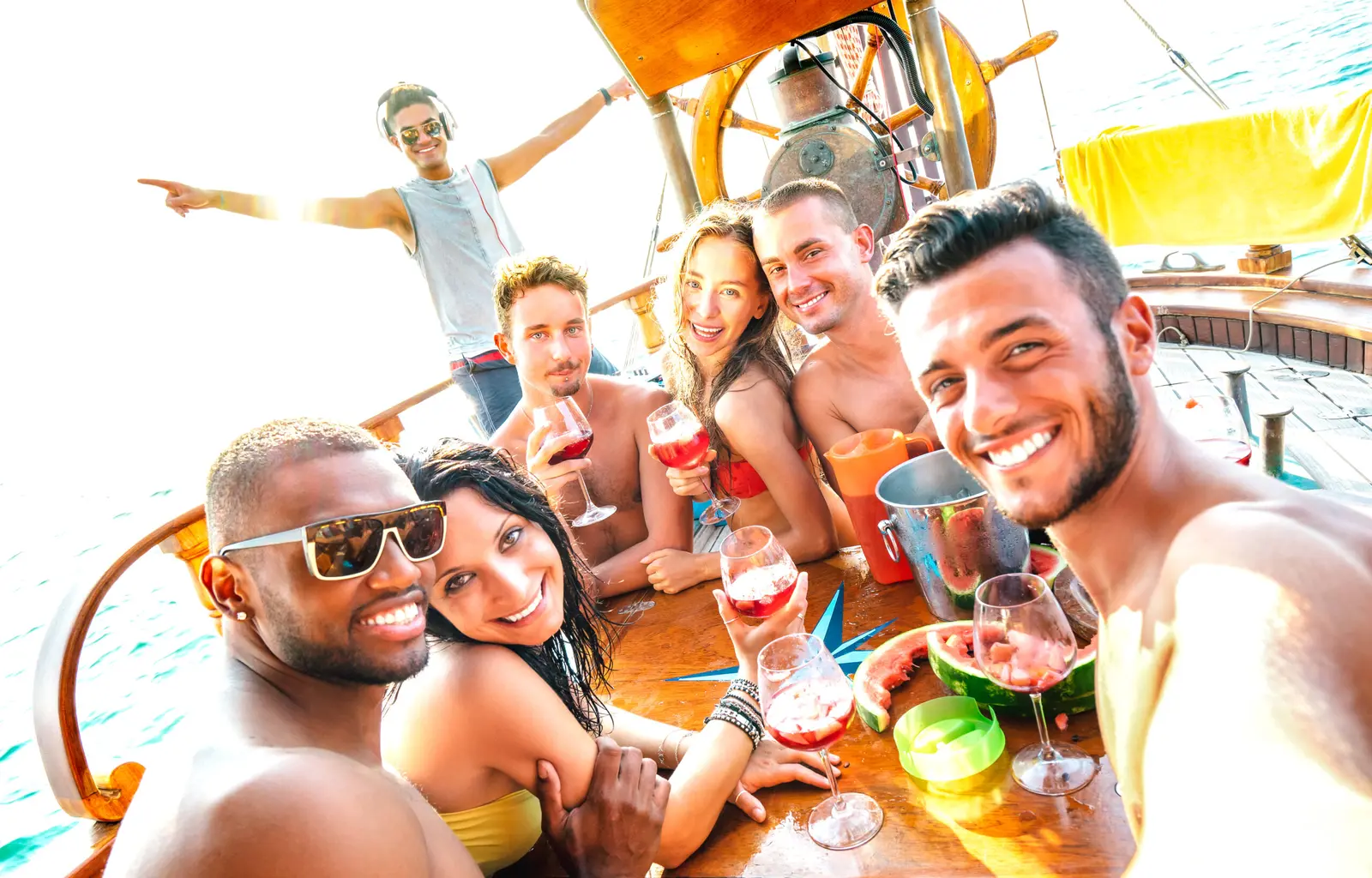 Guests with wine glasses taking a selfie around a wooden table on the yacht deck