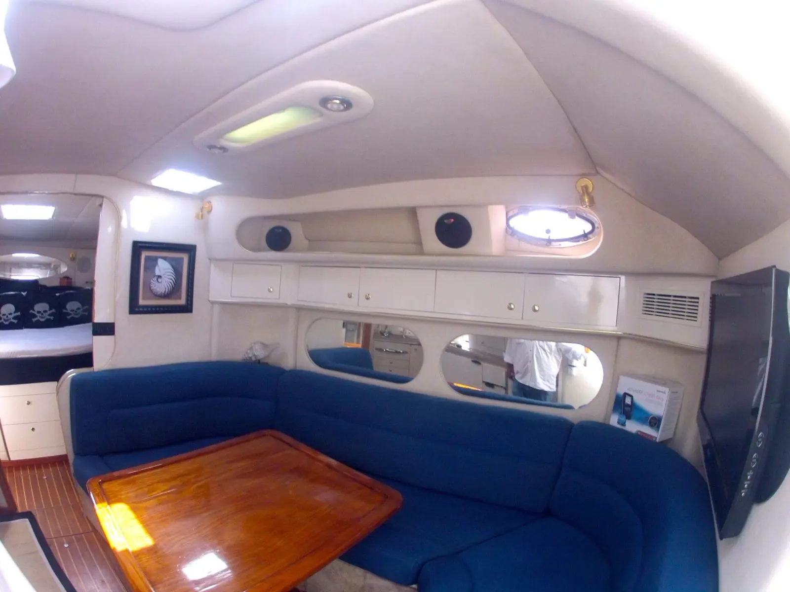 Yacht cabin with navy U-shaped seating around a polished wood table, portholes above