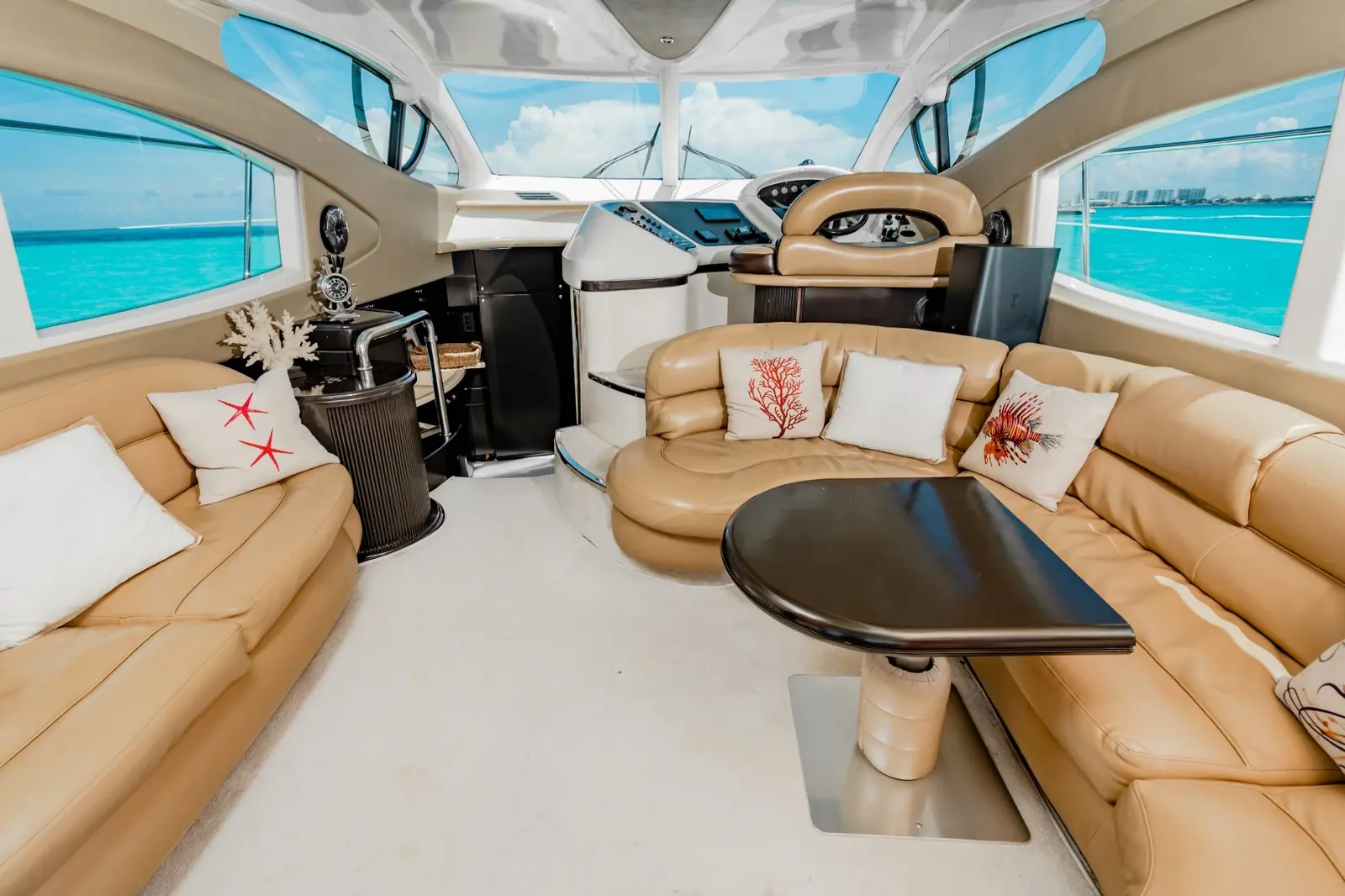 Tan leather lounge with coral-print cushions and the helm forward inside a motor yacht