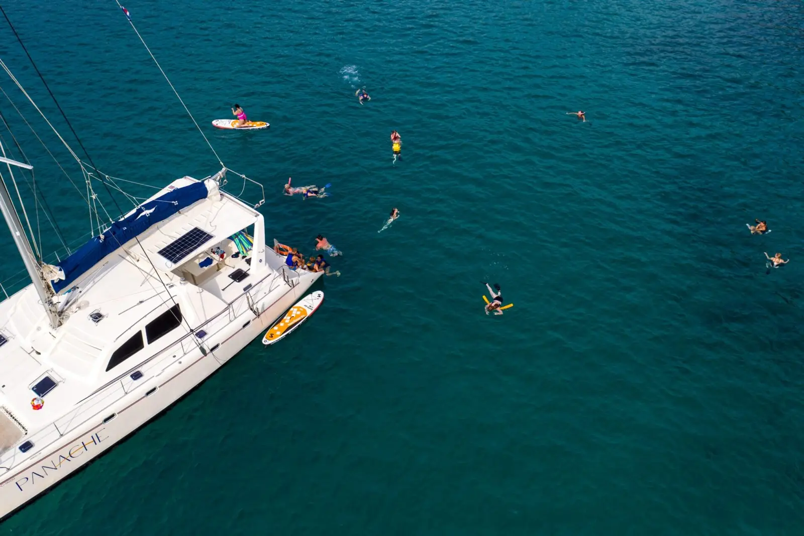 Aerial view of guests snorkeling and paddleboarding around the anchored sailing catamaran