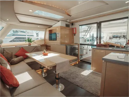 Sailing catamaran saloon with a dining table, red cushions and a galley beside the cockpit doors