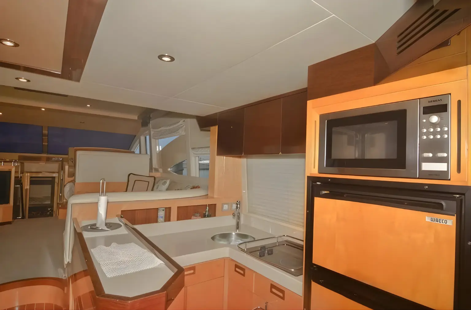 Yacht galley with wood cabinets, a microwave, oven and sink beside the dining area