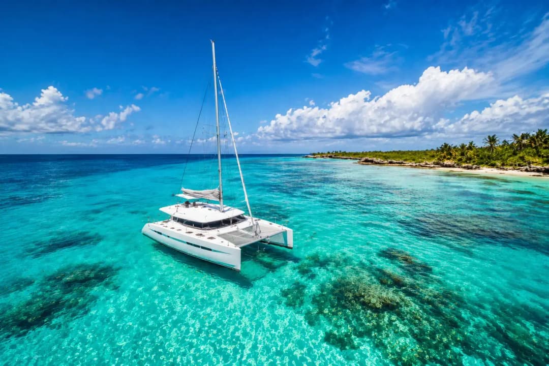 Best catamaran tours Cancun featuring a luxury white catamaran floating in crystal-clear turquoise water with visible coral reef and tropical shoreline