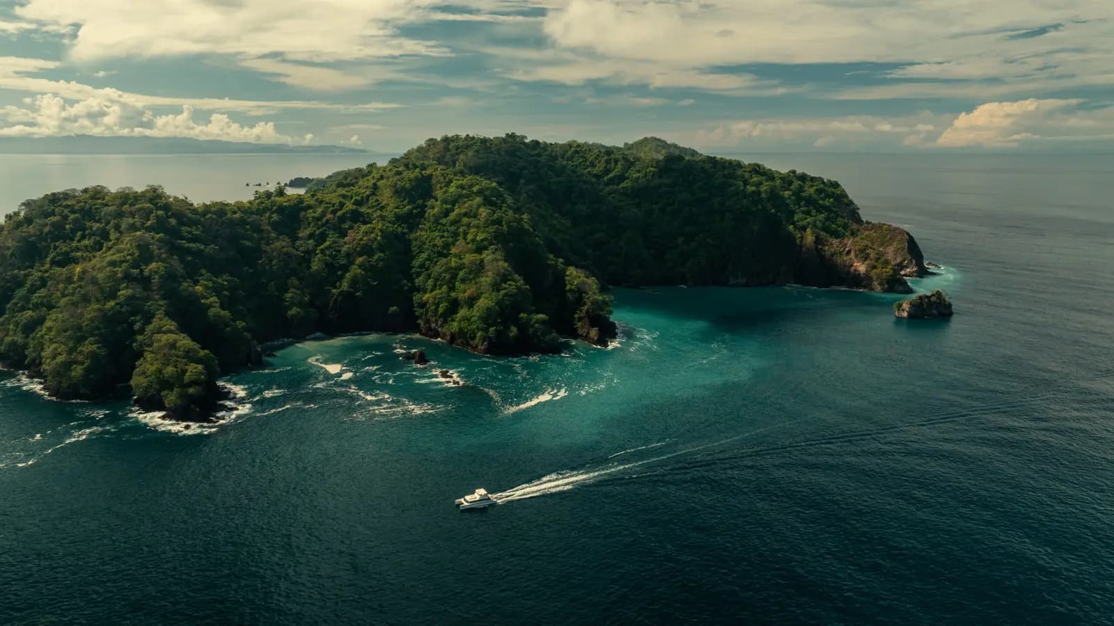 Aerial view of a speedboat trailing a white wake past a forested island in the Gulf of Nicoya