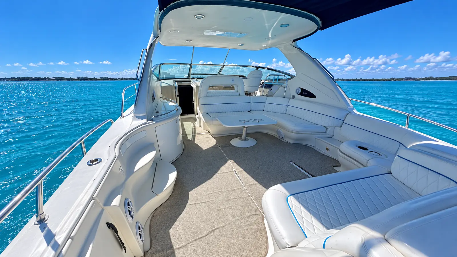 Open cockpit of a motor yacht with white wraparound seating under a radar arch on turquoise water off Cancún