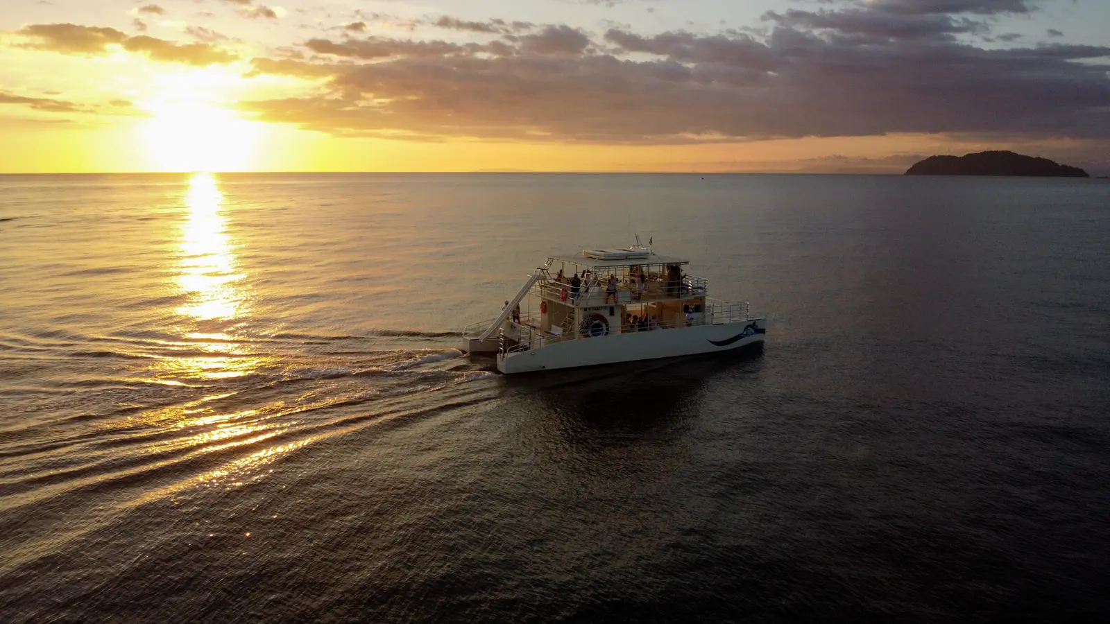 Two-deck catamaran cruising across calm water at sunset off Costa Rica's Pacific coast