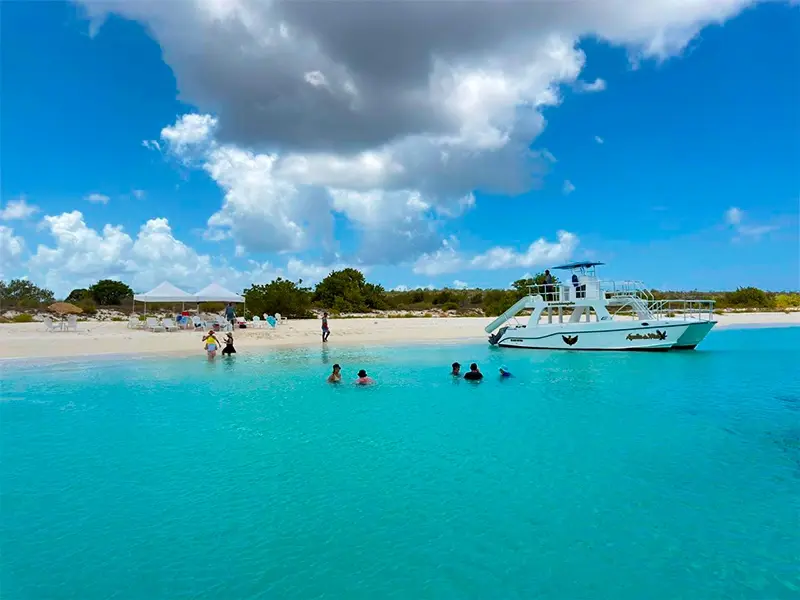 Catamaran anchored off a white-sand beach as guests swim in turquoise shallows at Bahía de las Águilas