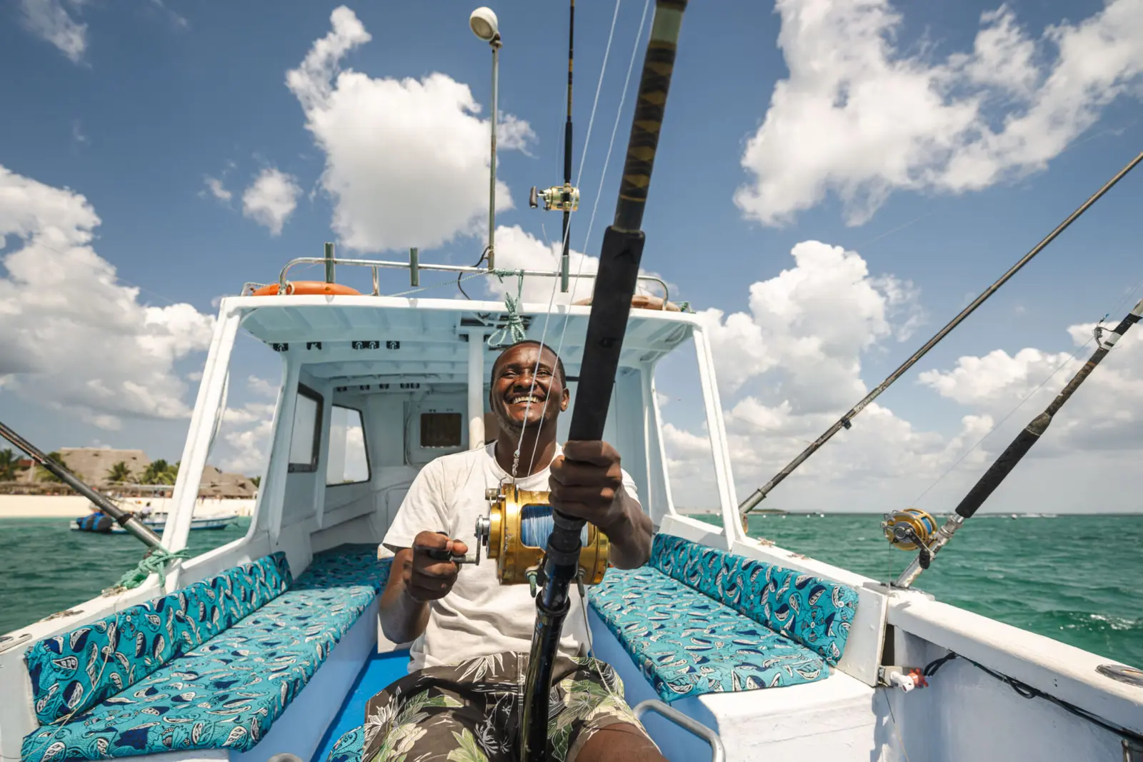 Smiling man holding a heavy rod and reel on the cushioned deck of a sportfishing boat off Zanzibar