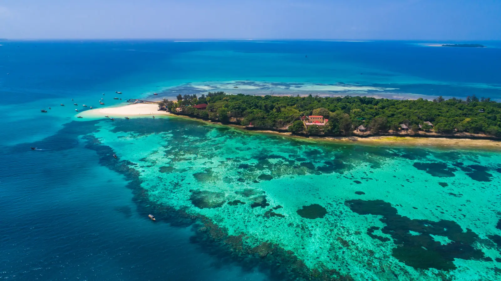 Wooded Prison Island seen from the air, a sandy spit at one end and coral reef all around