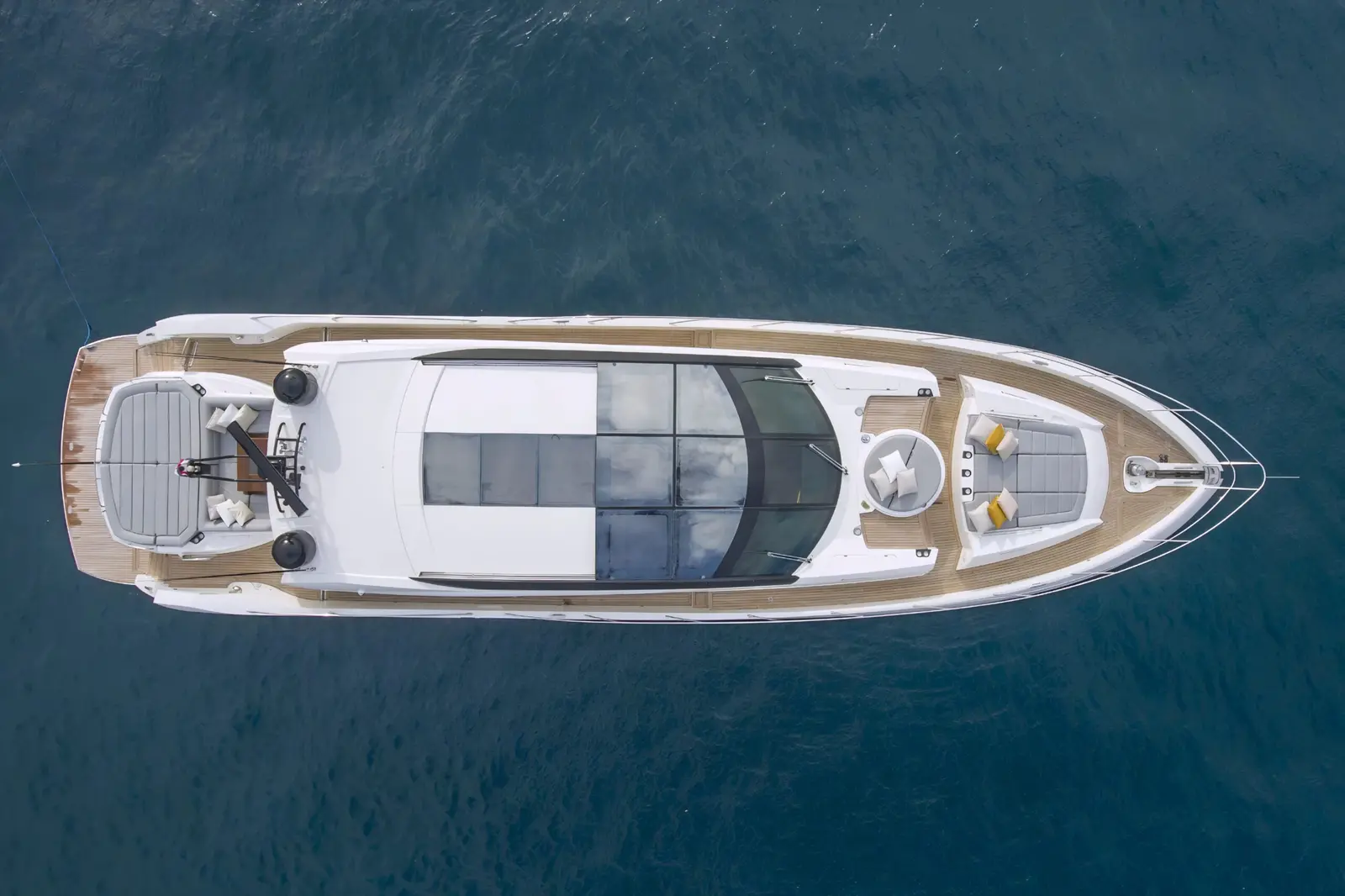 Top-down drone view of a motor yacht with teak decks and bow sunpads on deep blue water