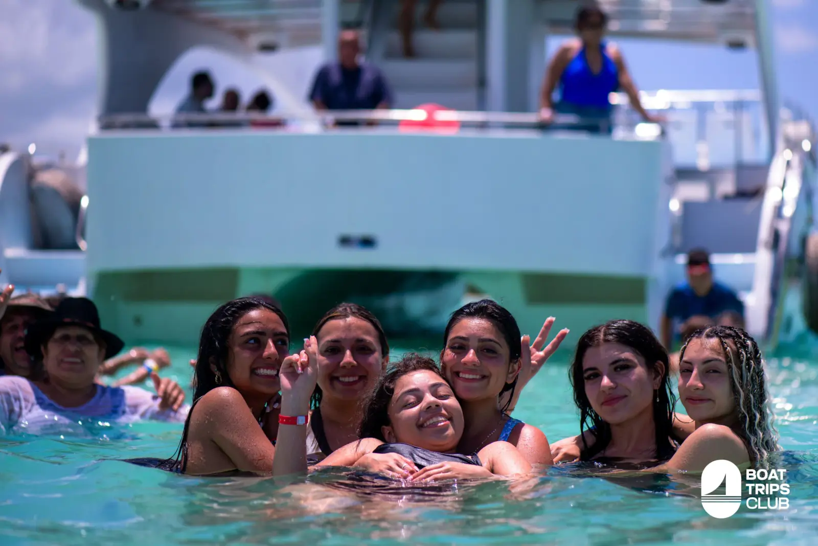 Smiling guests posing chest-deep in the water at the catamaran's stern