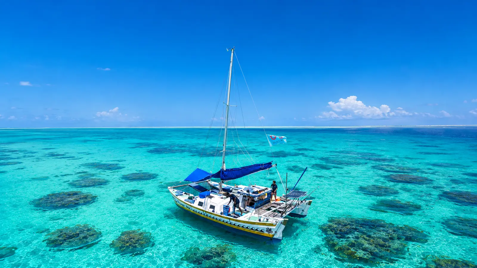 Sailing catamaran anchored over turquoise water dotted with dark coral patches off Zanzibar