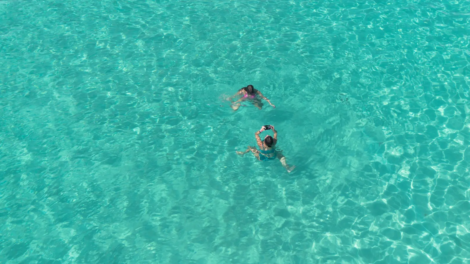 Two swimmers in clear turquoise water off Punta Cana, seen from directly above