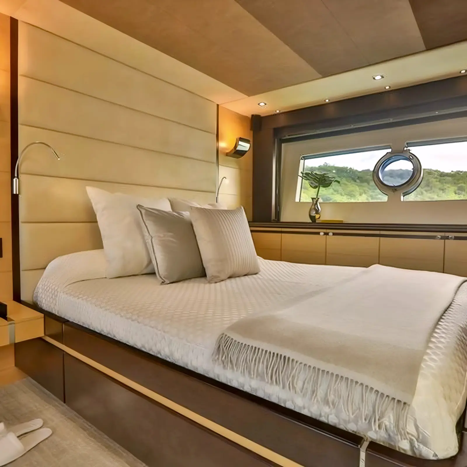 Guest cabin with a double bed, folded throw and a long hull window framing a green shoreline