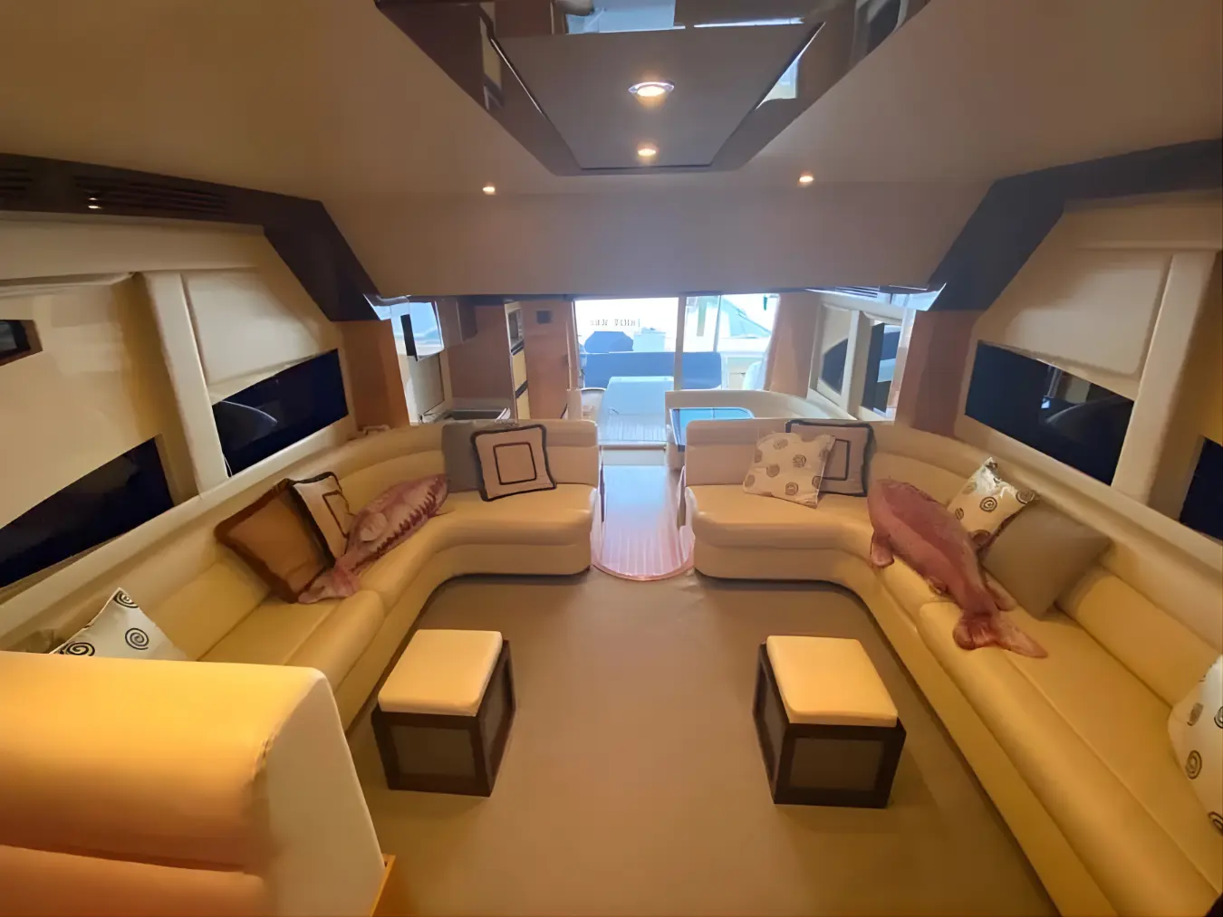 Salon with two facing beige sofas and ottomans, glass doors opening to the aft deck