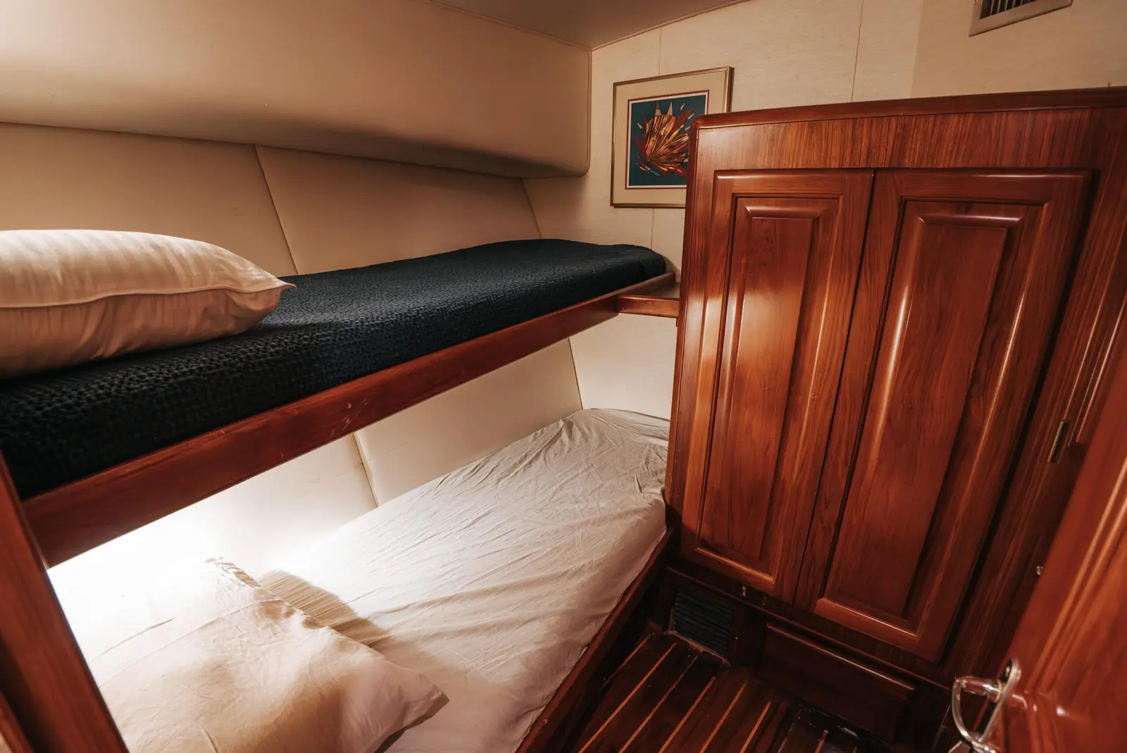 Yacht guest cabin with upper and lower bunks and glossy wood cabinetry