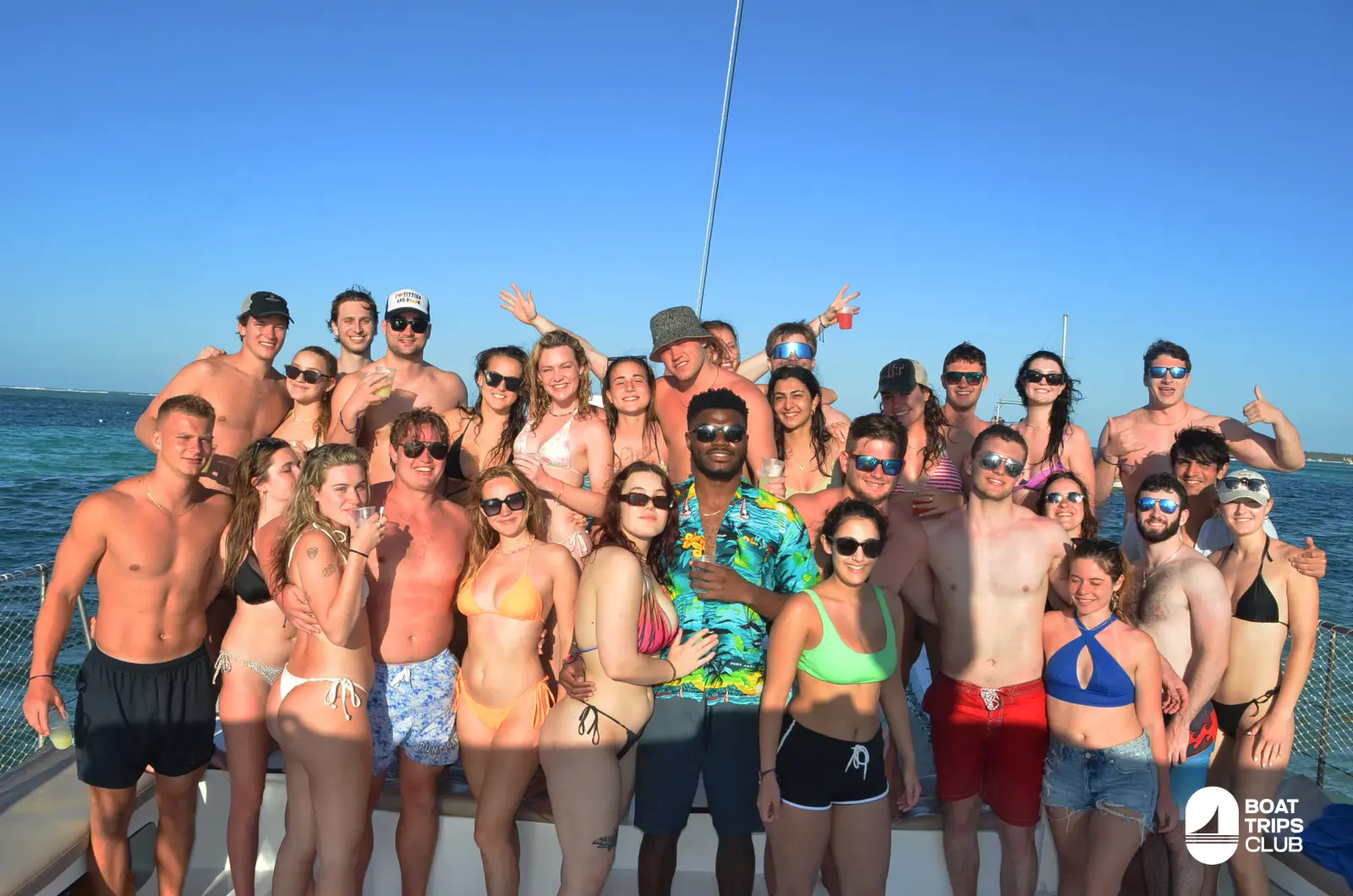 A large group of friends in swimwear pose together on the deck of a sailing catamaran