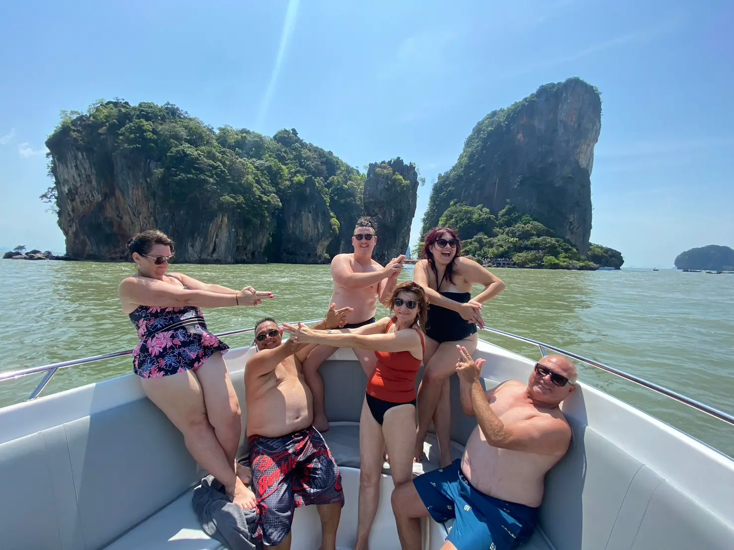 Group of guests striking finger-gun poses on the speedboat bow among the karst islands of Phang Nga Bay