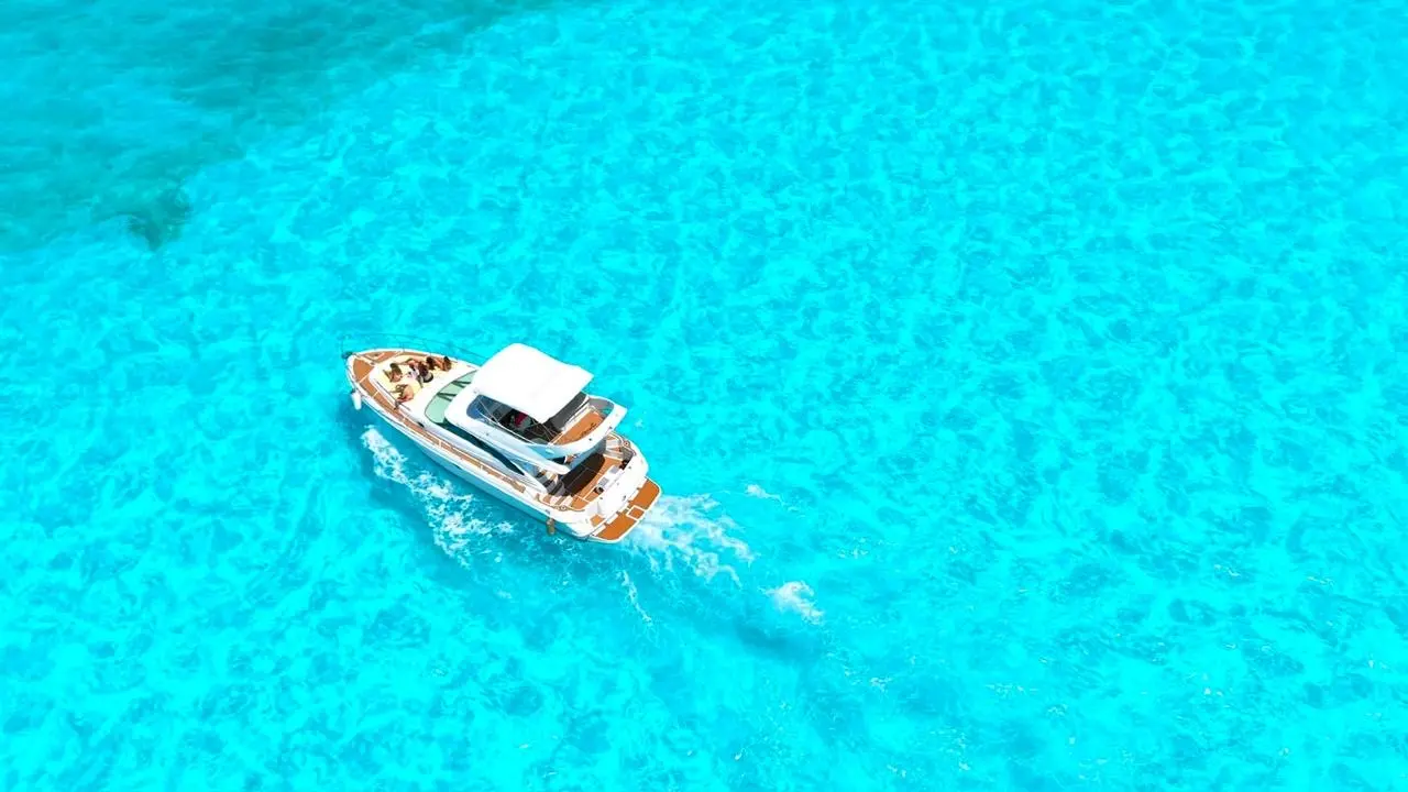 Aerial view of a flybridge yacht cruising across bright turquoise water off Cancún