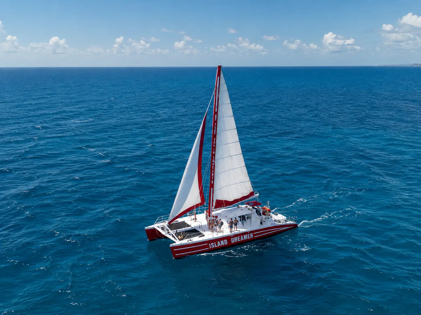 Red and white sailing catamaran under full sail on deep blue water off Montego Bay, seen from above