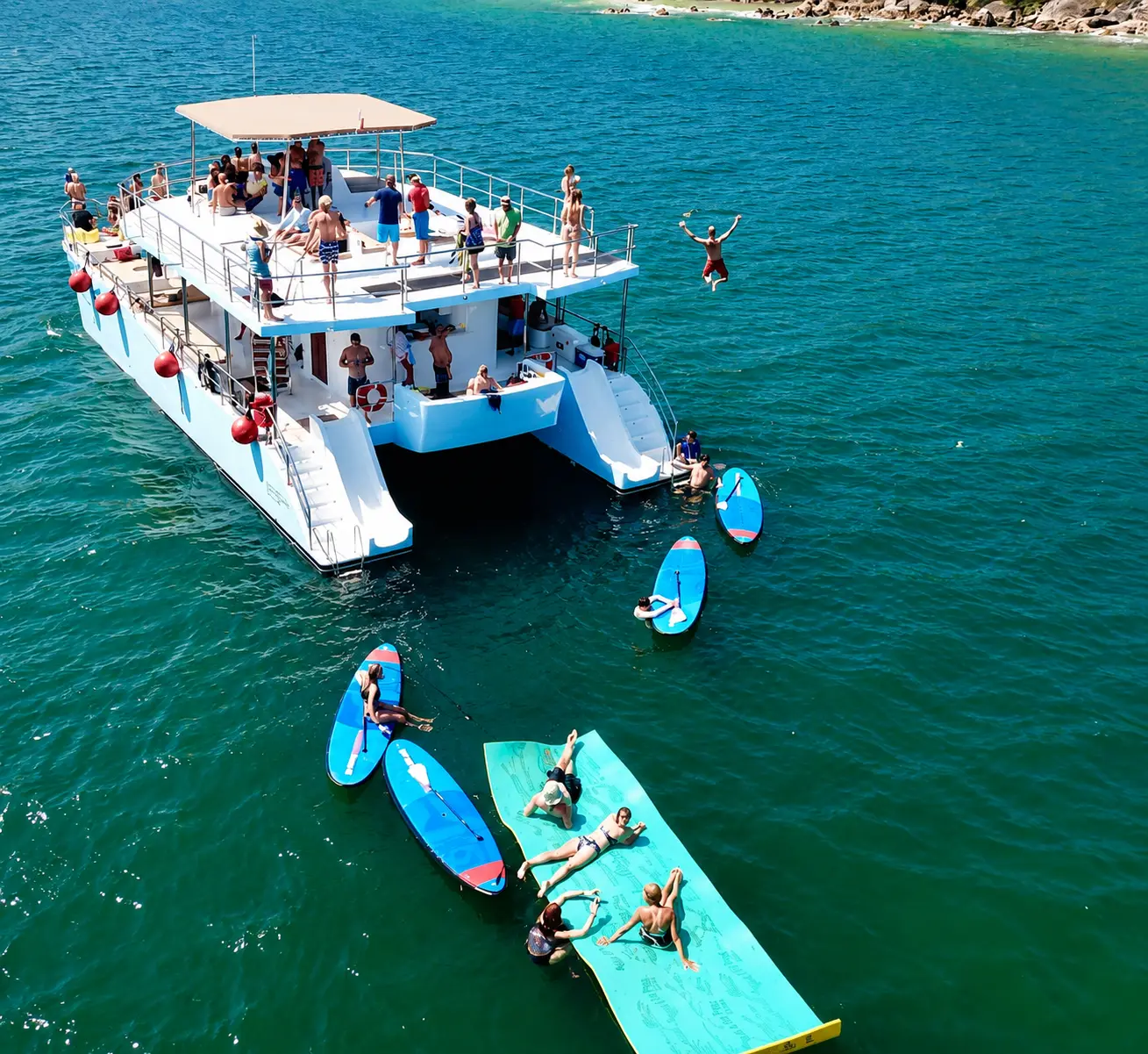 Aerial view of a two-deck catamaran anchored off Puerto Vallarta, guests on paddleboards and a floating mat