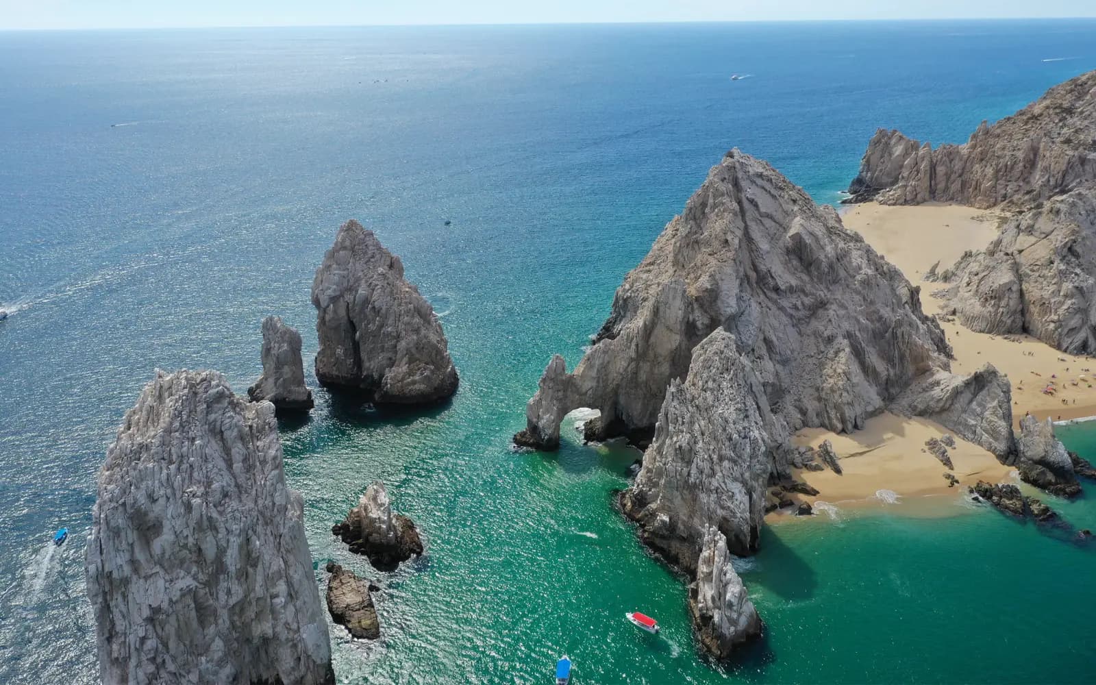Aerial view of granite pinnacles beside Lover's Beach with small boats in turquoise water