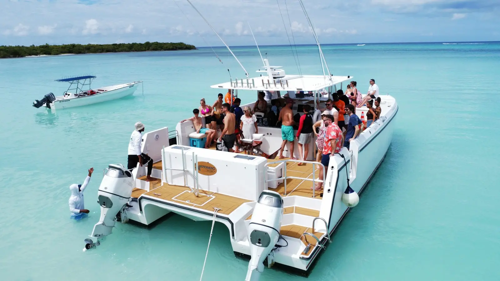 Guests crowd the aft deck of a power catamaran anchored off Saona Island, a speedboat moored nearby