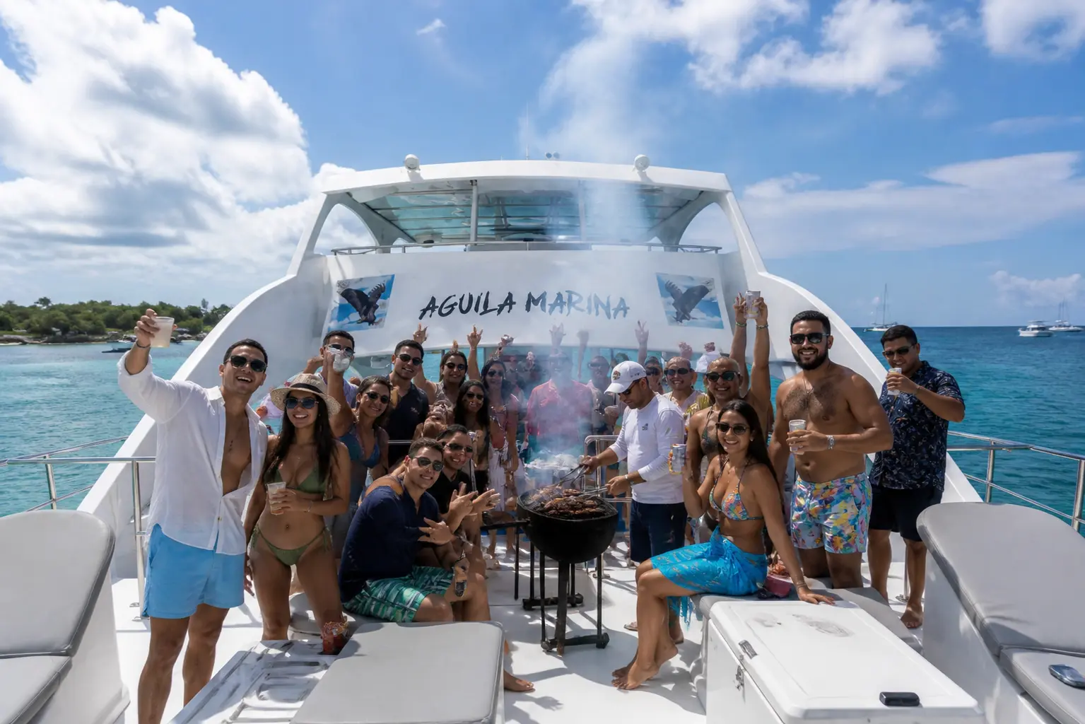 Group of guests posing on the catamaran's sunny front deck beside a smoking grill