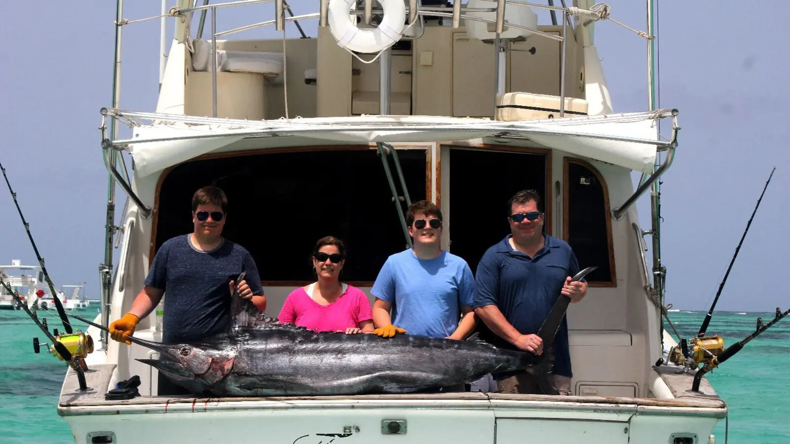 Four anglers posing with a billfish across the transom of a sportfishing boat, flybridge above