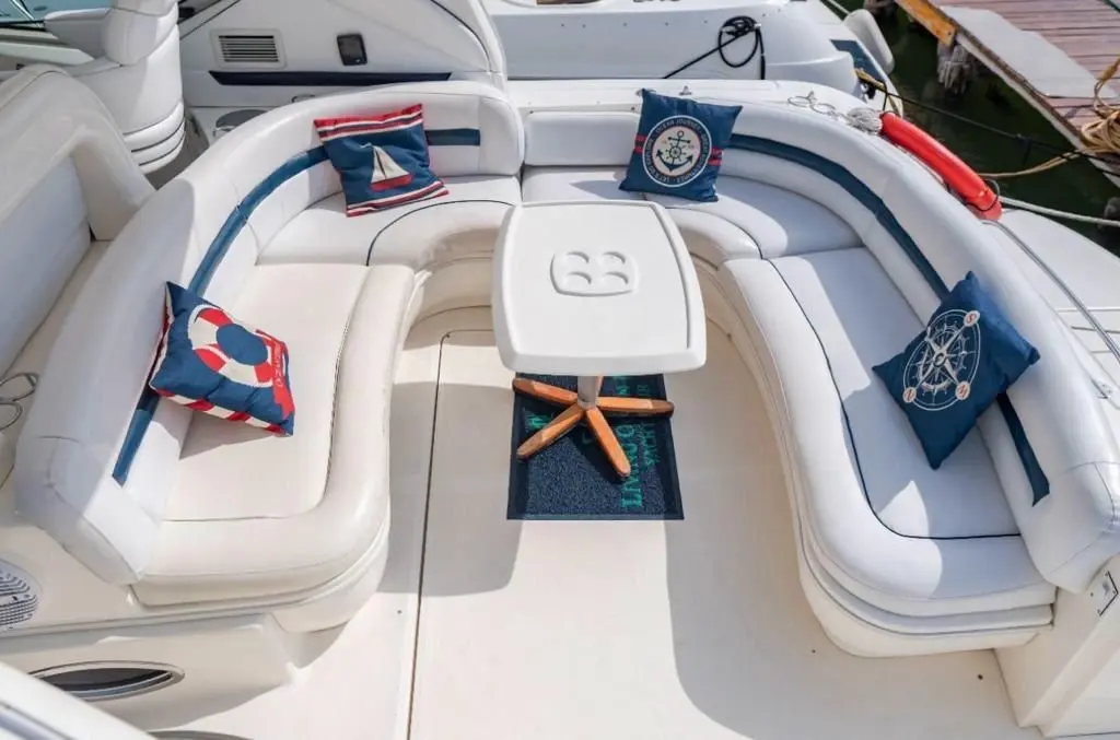 Yacht cockpit lounge with white U-shaped seating, navy nautical pillows and a small table