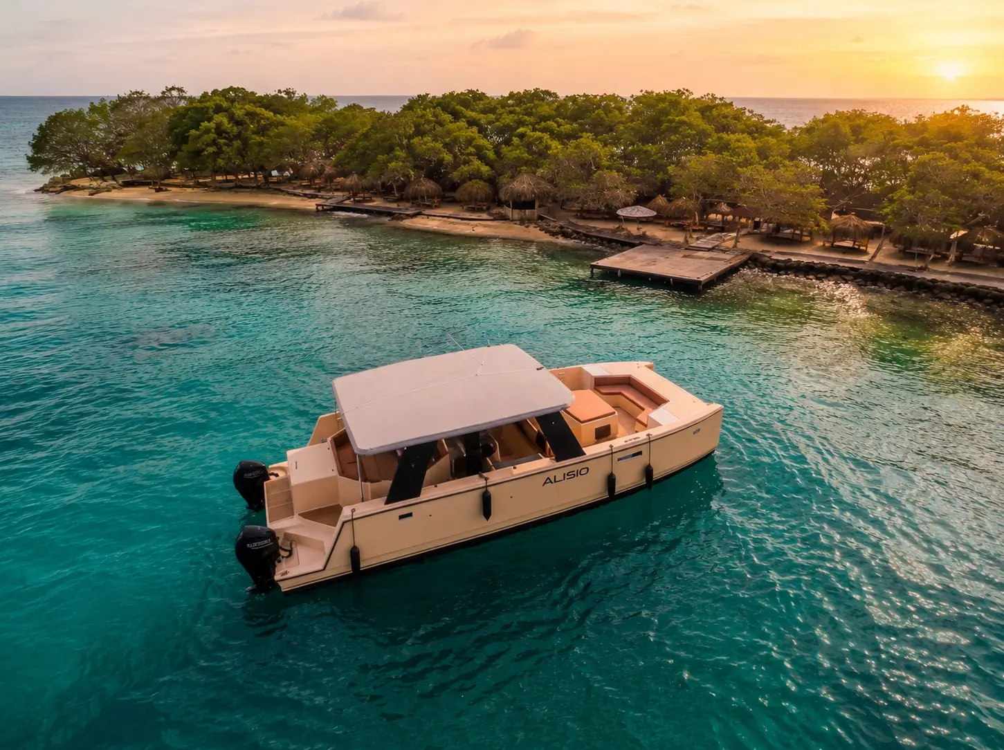 Cream power catamaran with a white hardtop anchored off a wooded island and pier in the Rosario Islands at sunset